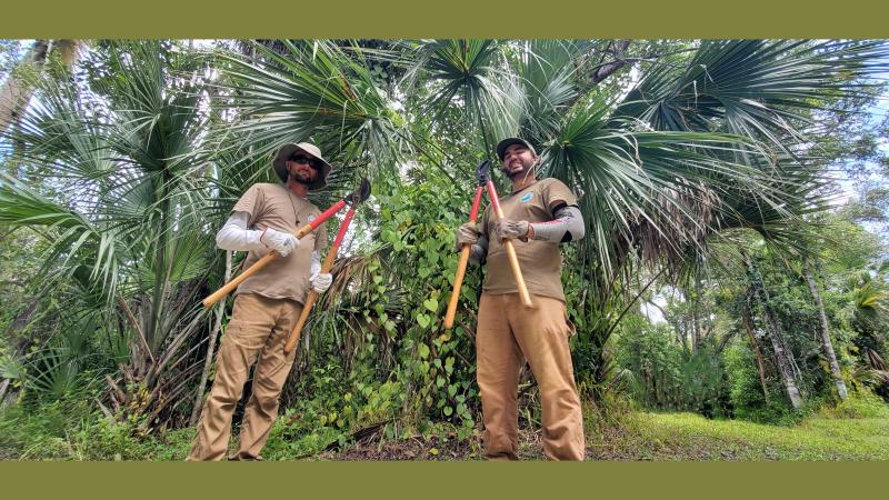 Two people standing holding loppers in a wooded area.