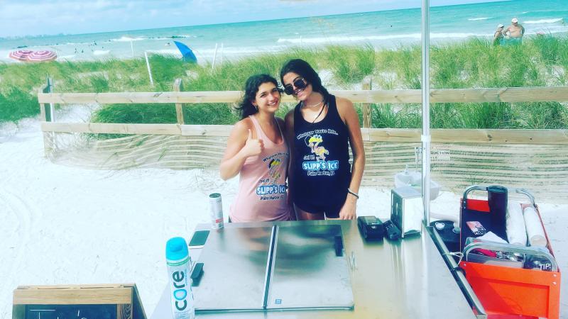 Two women pose with the ice cart at the beach.